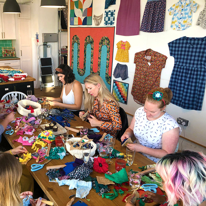 Participants of a rag rug class. The table in front of them is full of fabric