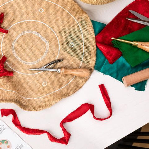 Workshop setup for creating a Christmas wreath with materials such as fabric, scissors, and ribbons laid out on a table.