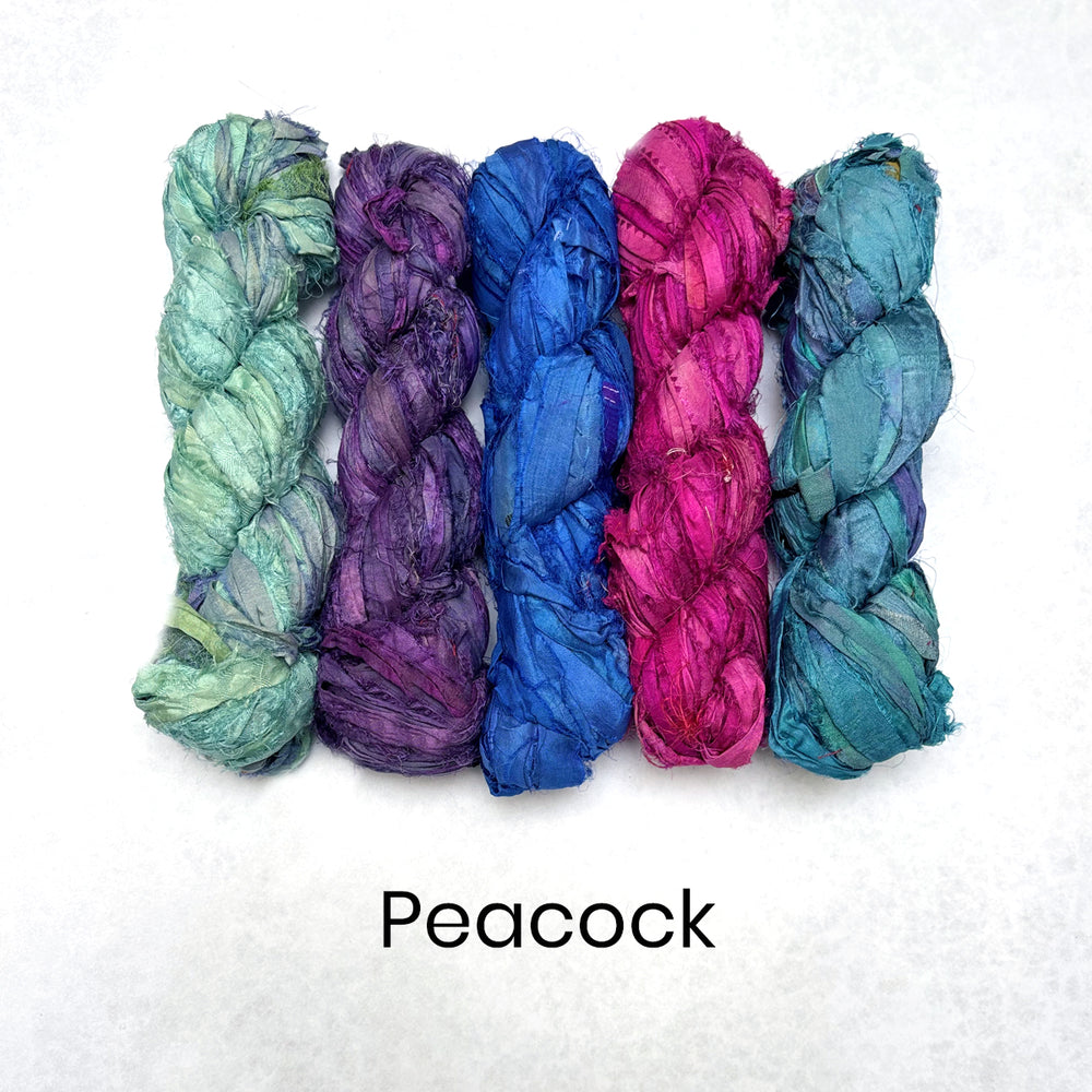Five skeins of colorful yarn in shades of green, purple, blue, and pink on a white background with 'Peacock' text.