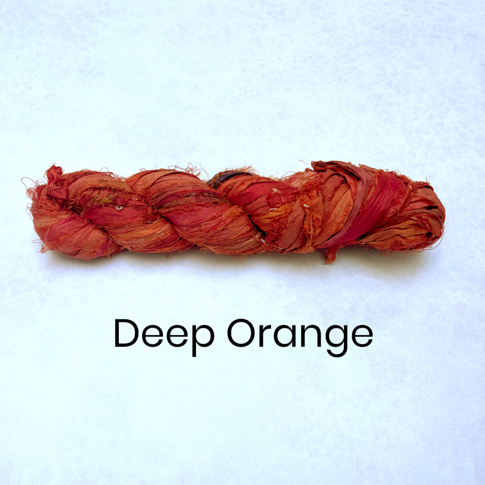 Braided skein of deep orange recycled sari silk ribbon sari remnants on a light blue background with 'Deep Orange' text.