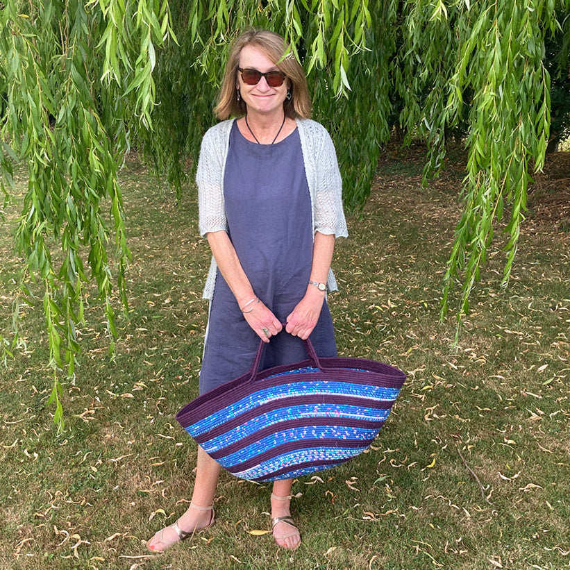 Woman holding a handmade coiled rope striped basket under a willow tree