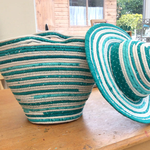 Teal and white striped basket and coiled rope hat on a wooden surface 