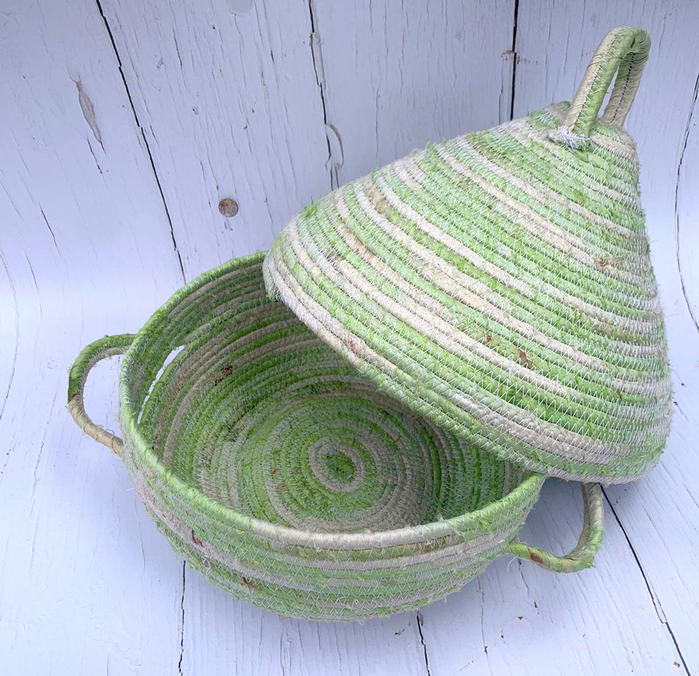 Green and beige coiled rope handmade basket with a lid on a light wooden surface