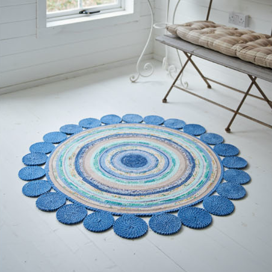 Round blue rag rug on a white floor with a bench in the background made using cotton cord and stitched on a sewing machine 