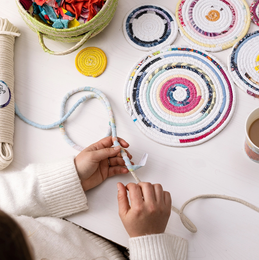 Person making a colourful coiled rope table runner using cotton cord and fabric strips. 