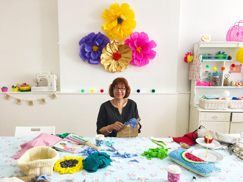 Person sitting to make a rag rug with brightly coloured fabric flowers surrounded them
