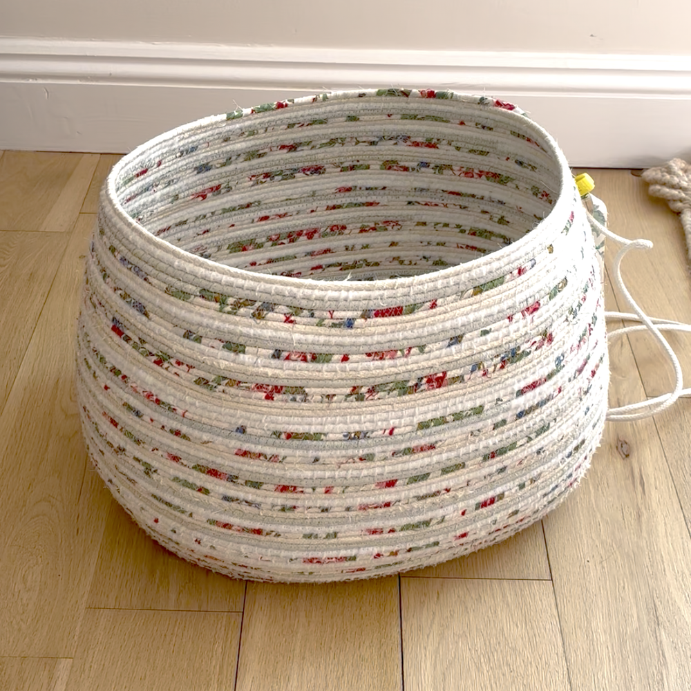 Woven fabric basket with floral pattern on a wooden floor made using rope coiling technique