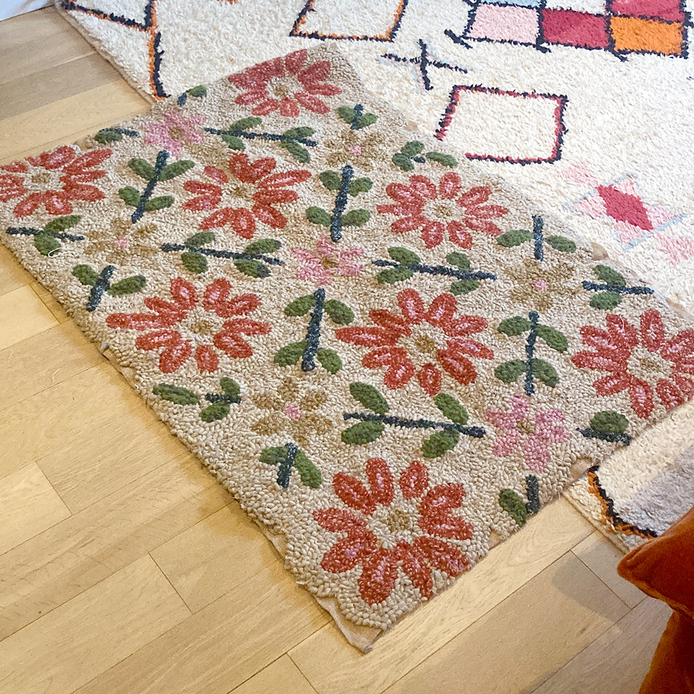 Floral patterned handmade rug hooked rag rug on a wooden floor with another rug in the background.