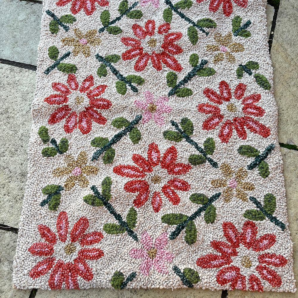 Floral patterned handmade rag rug with red, green, and pink flowers on a textured surface