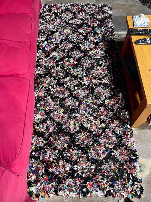 Multicolored shaggy rug on a carpeted floor next to a pink couch and wooden coffee table.