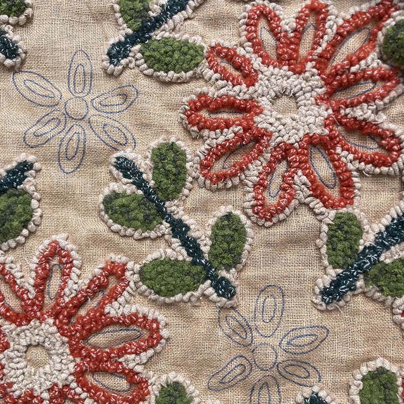 Close-up of rug hooked flowers with orange, green, and white on a hessian / burlap rug backing 