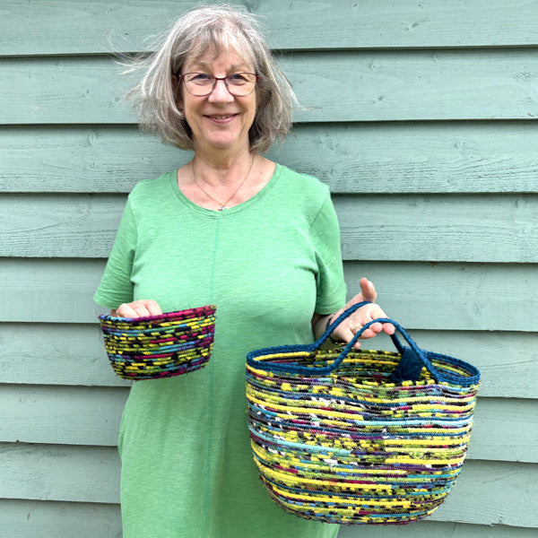 Woman holding two colorful handmade cotton cord stitched baskets against a light green wooden wall