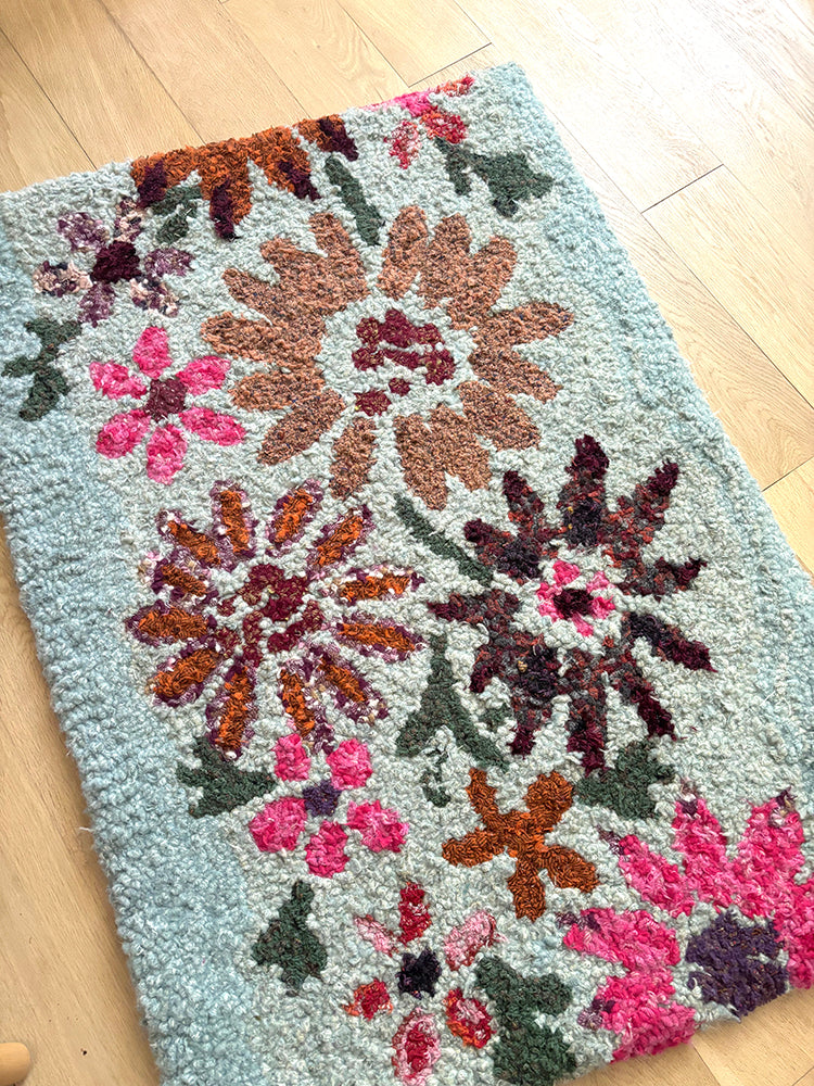 Wildflower Meadow Design Floral patterned rug hooked rag rug on a wooden floor with a blue background and autumn coloured flowers