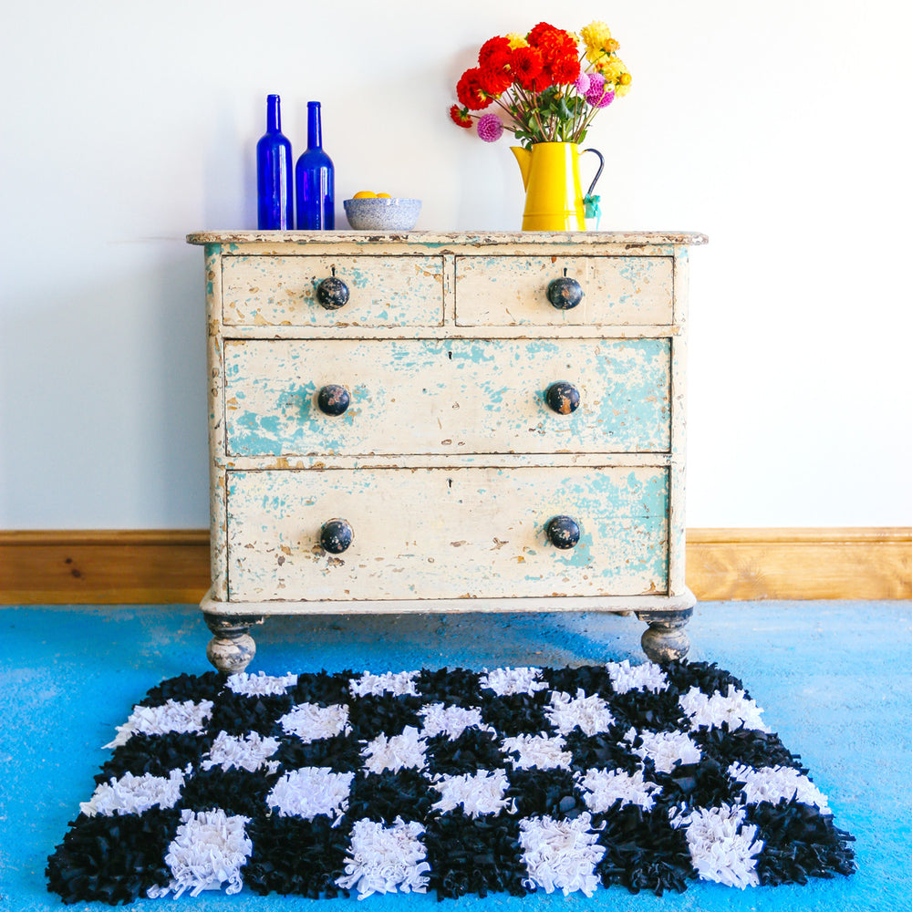 Black and white shaggy checked handmade rag rug inside on a blue floor in front of a chest of drawers display