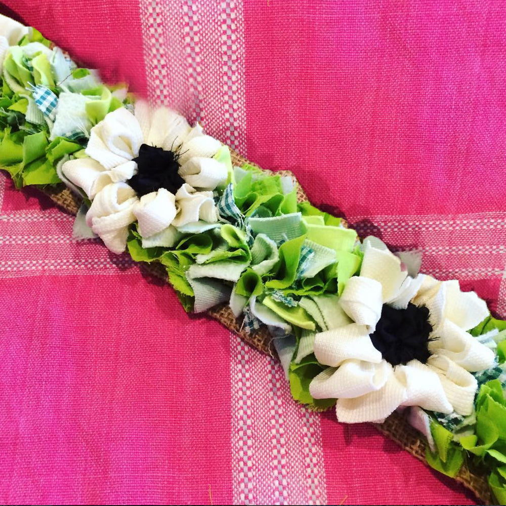Rag rug handmade loopy and shaggy green and white flower trim against a pink fabric background