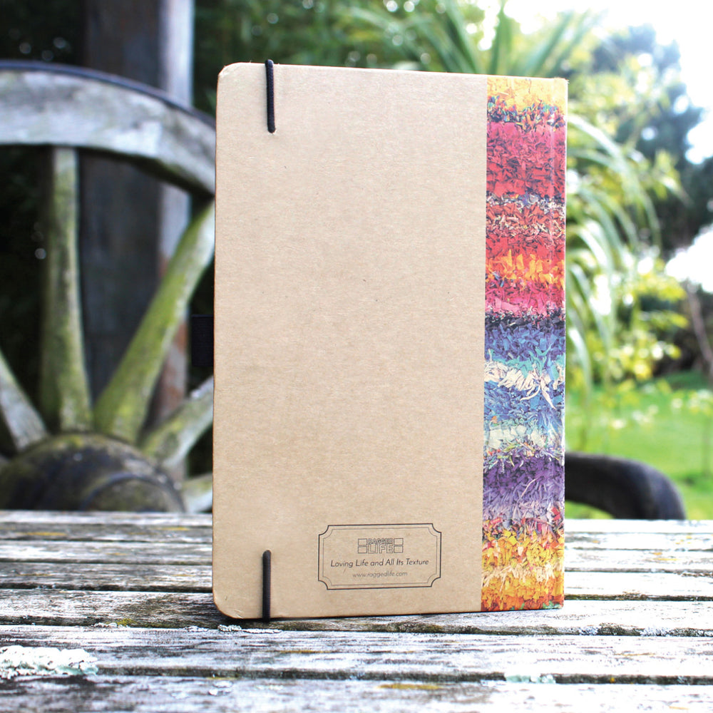 Ragged Life hardback notebook with brown cover and colourful rainbow rag rug image with an elastic hold