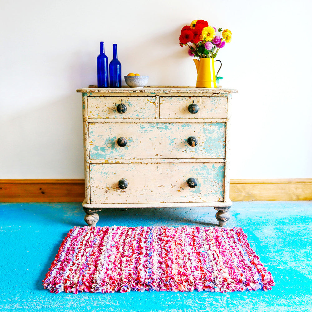 Handmade Pink Striped Shaggy Rag Rug on a blue floor in front of a chest of drawers