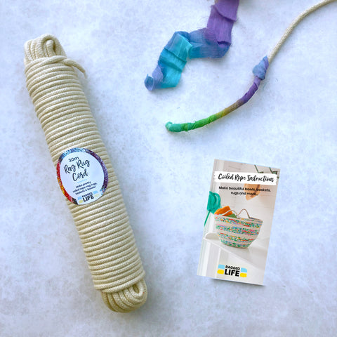 A 30 metre skein of cream cotton cord is displayed alongside a piece of coiled rope rag rug in progress and a booklet with instructions.