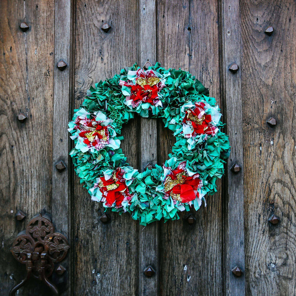 Festive Christmas handmade green and red holly flower rag rug wreath hanging outside on a wooden door 