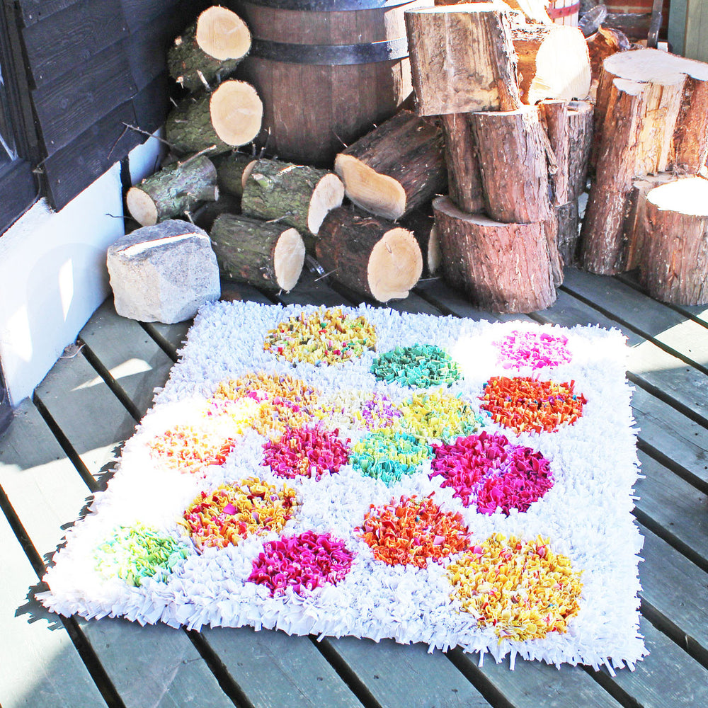 Shaggy rag rug with a colourful polka dot pattern on a white background displayed outside on a wooden barn floor